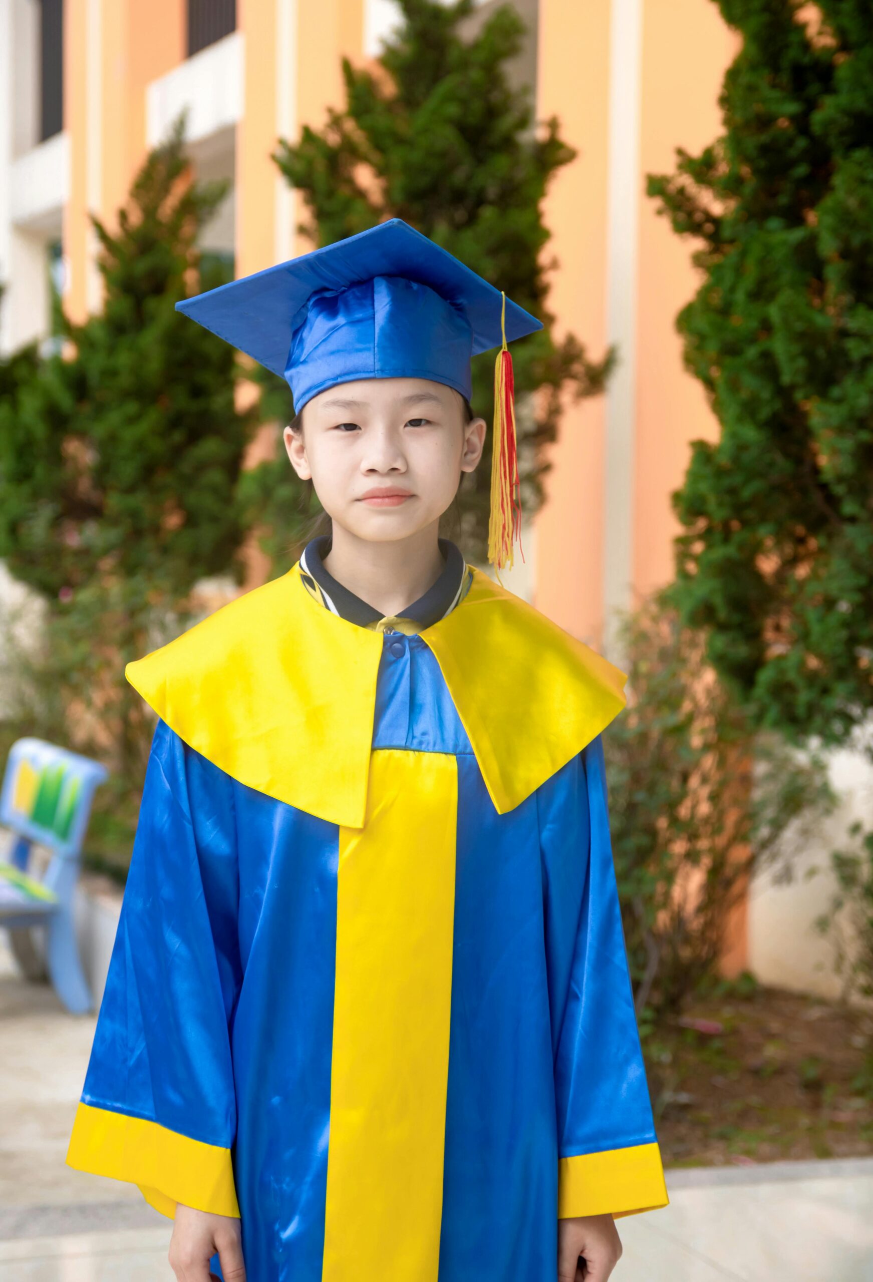 A child wearing a vibrant blue and yellow graduation outfit standing outdoors.