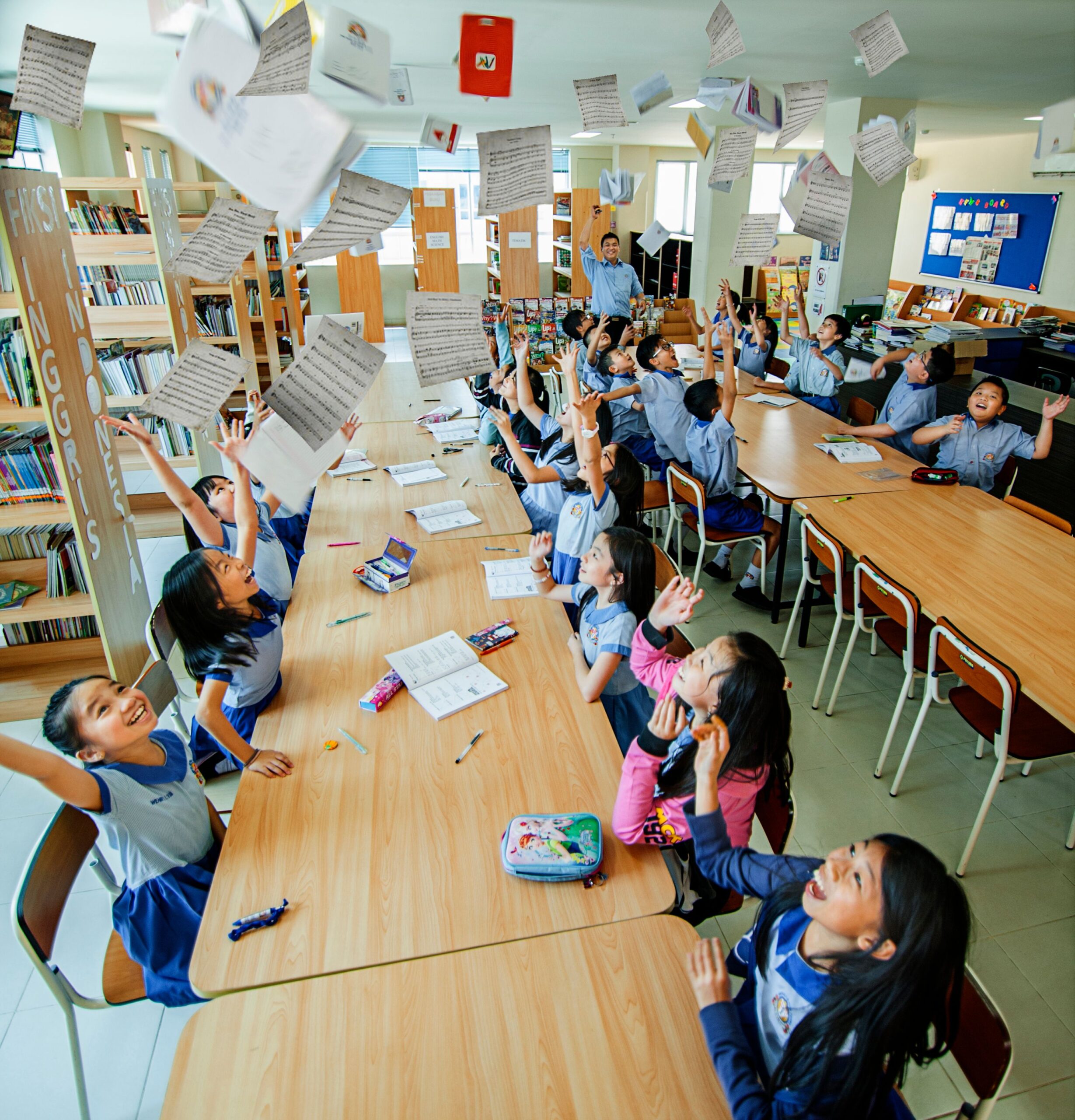 Joyful students in a classroom celebrating by throwing papers and having fun together.